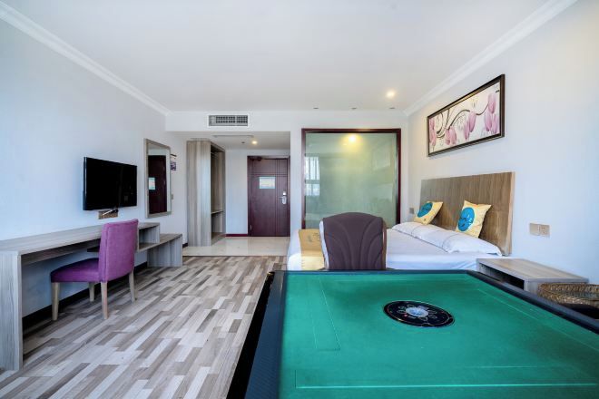 A hotel room with a pool table, a TV, a desk with a chair, a bed with pillows, and a door leading to another room.