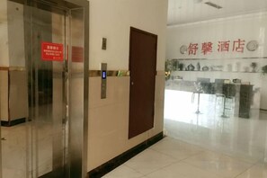 Eine Hotelhalle mit einer Rezeption, einem Glaselevator und einer Tür mit einem roten Schild.