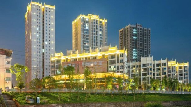Un complesso residenziale a grattacielo al crepuscolo, con finestre illuminate e un'area verde curata di fronte.