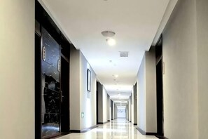 A long, narrow hotel corridor with a polished floor, dark-framed glass doors, and recessed lighting. - lemon hotel (Chongqing)