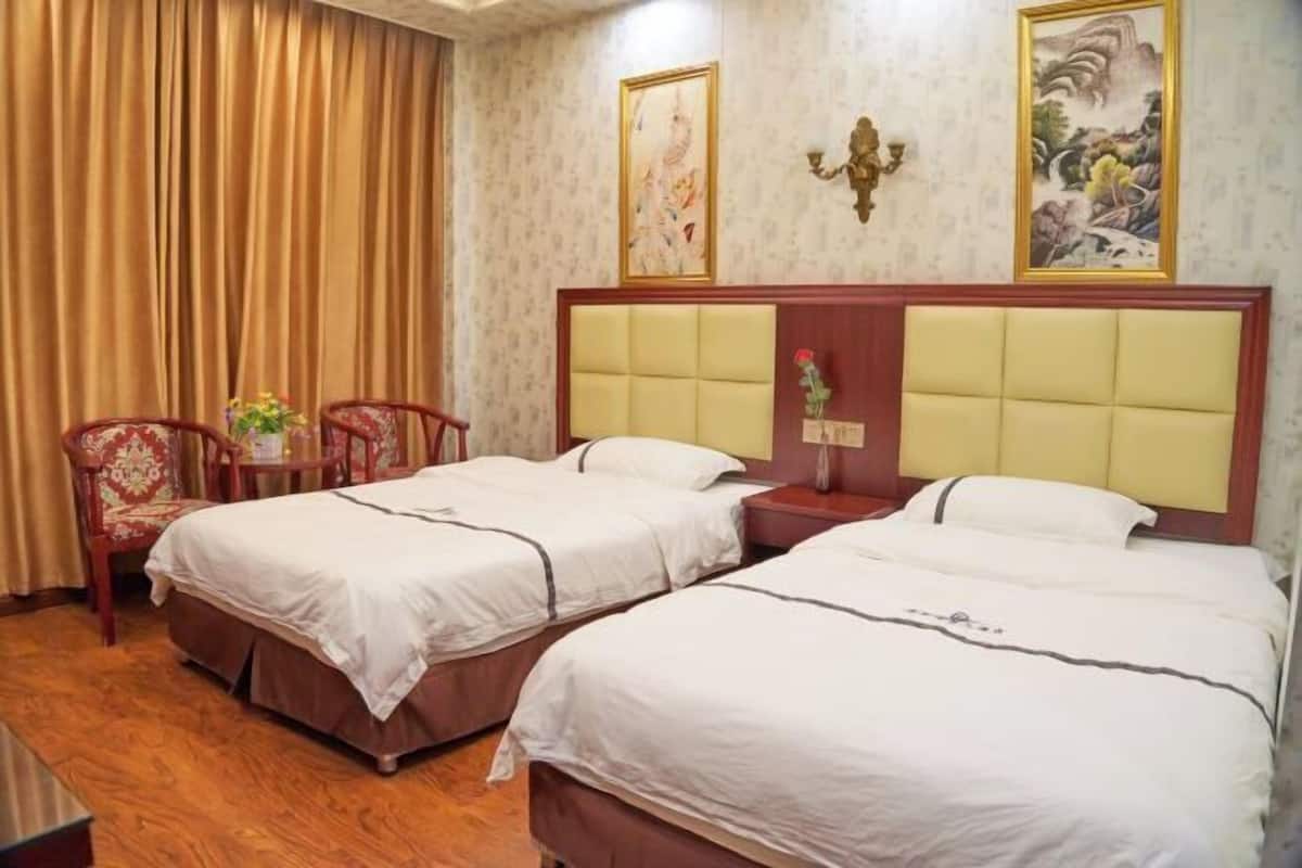 A hotel room with two beds, a wooden desk, a chair, and a curtain.