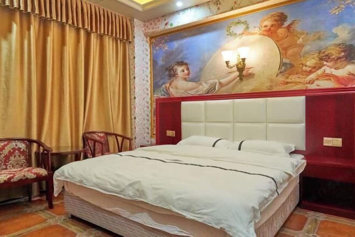 A bedroom with a large bed, a headboard, a wall mural, and a pair of chairs.