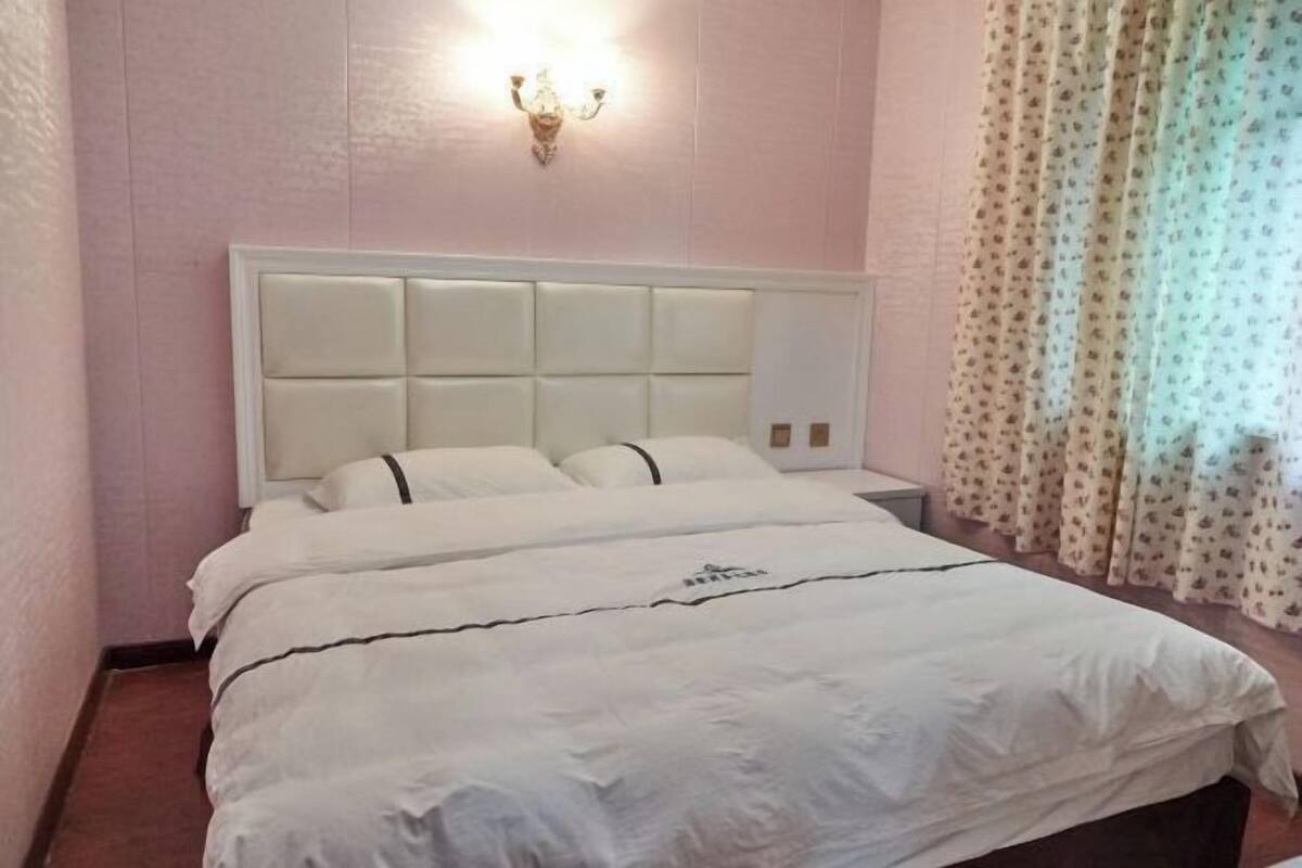 A bedroom with a white headboard, a bed with white bedding, a nightstand, and a wall-mounted light fixture.