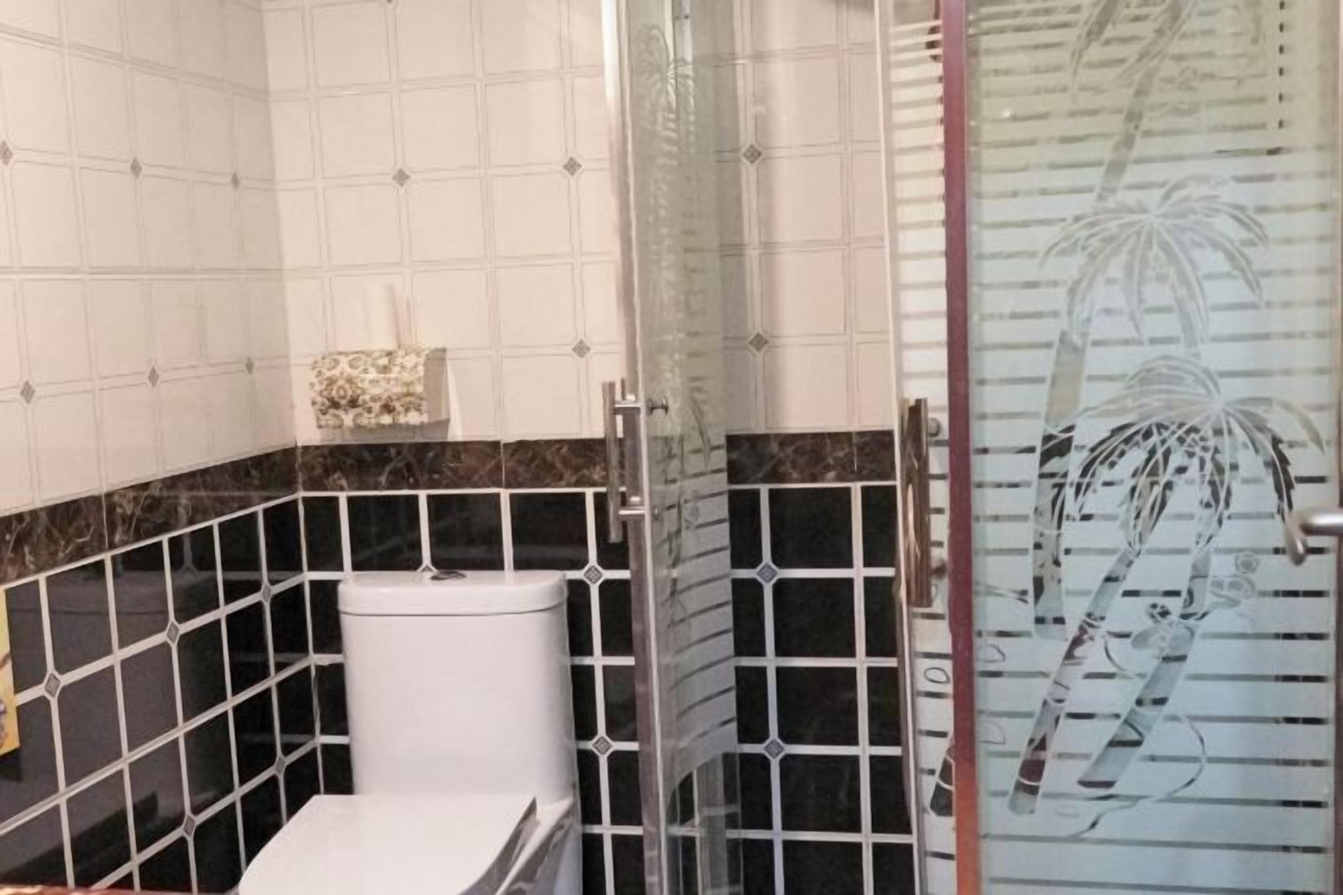 A bathroom with a toilet, a shower area, and a glass door with a palm tree design.