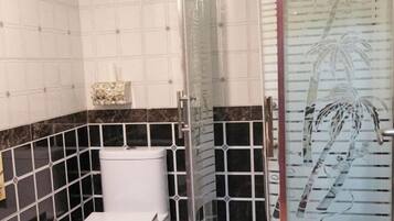 A bathroom with a toilet, a shower area, and a glass door with a palm tree design.