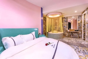 Una habitación de hotel con una cama, una mesita redonda, un espejo y un baño con lavamanos e inodoro.