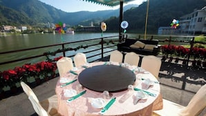 An outdoor dining area with a round table set for six, surrounded by chairs, overlooking a lake with mountains in the background. - Lakeside Resort (Nantou)