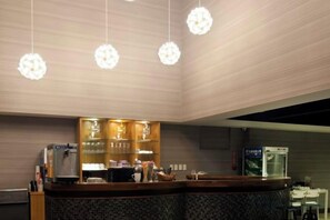 Zona de recepción de un hotel con mostrador, máquina de café y dispensador de agua.