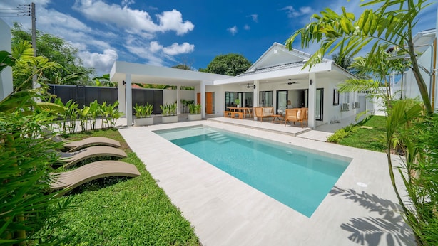 Une maison moderne dotée d’une piscine, de mobilier d’extérieur et d’une végétation luxuriante.