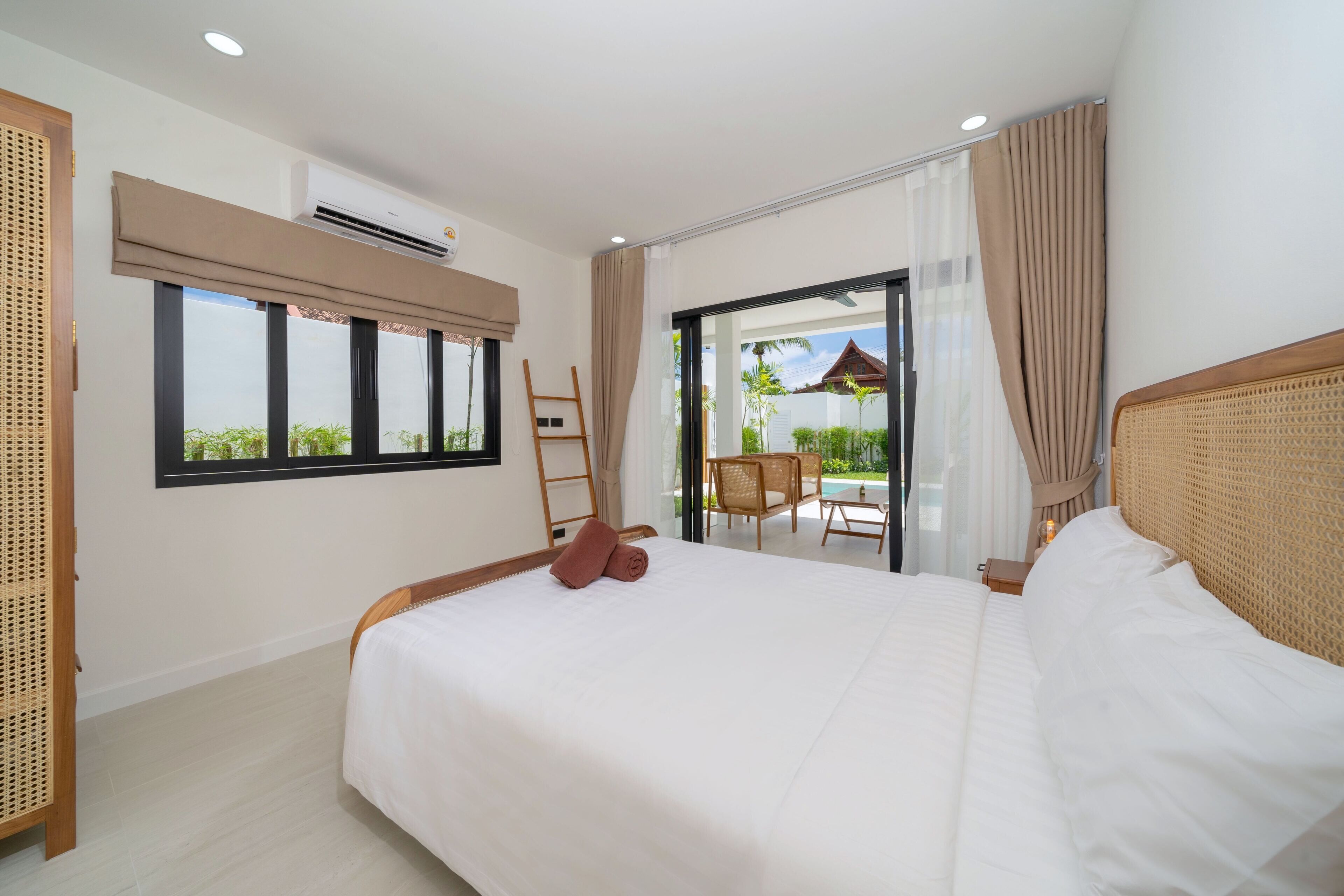 Une chambre d’hôtel avec un grand lit, une fenêtre avec des stores, un balcon avec une chaise et une échelle en bois.