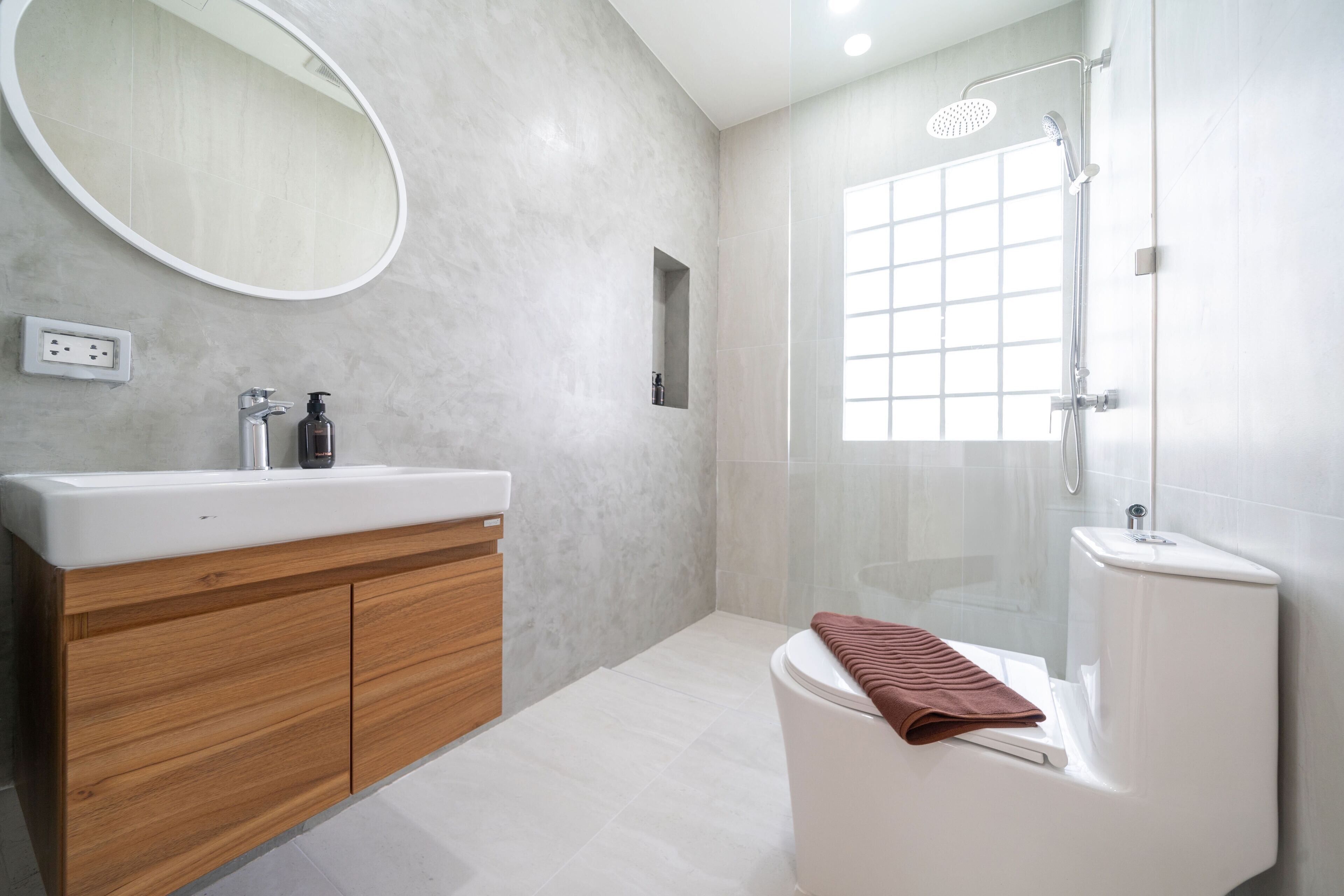 A modern bathroom with a wooden vanity, a white sink, a mirror, a shower enclosure, and a toilet.