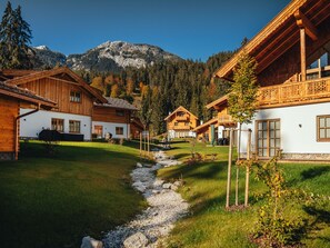 Un hilera de cabañas de madera con paredes blancas, frente a un paisaje de montañas y árboles.
