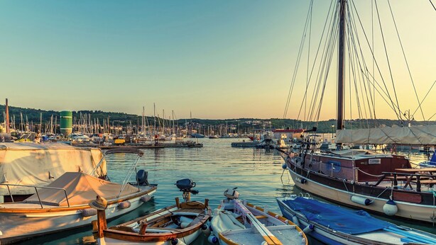 Un port de plaisance où sont amarrés différents bateaux, un pont en arrière-plan et une vue lointaine d’une ville.