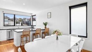 Een moderne keuken met een groot raam, een eethoek met een witte tafel en stoelen, en uitzicht op woningen.