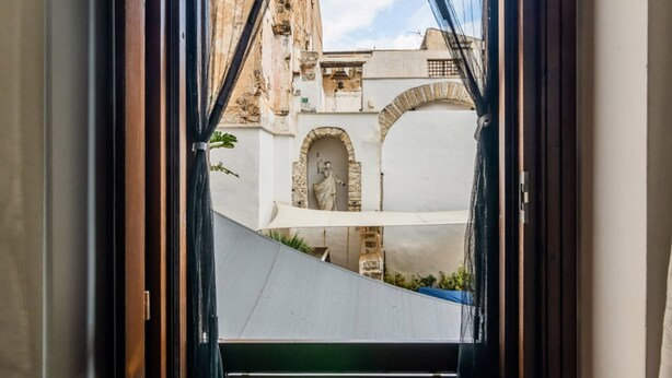 A view through a window with a white awning, a stone statue, and an arched doorway. - GuestHost - Cozy apartment of 80 sqm, on two levels, for 2 people, located on the 1st floor of a building with lift (steps to access: not suitable for disabled people).The property is located in the heart of the historic center of Palermo (Restricted Tra (Palermo)