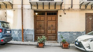 A building with a double wooden door, potted plants, and a car parked on the street. - GuestHost - Cozy apartment of 80 sqm, on two levels, for 2 people, located on the 1st floor of a building with lift (steps to access: not suitable for disabled people).The property is located in the heart of the historic center of Palermo (Restricted Tra (Palermo)