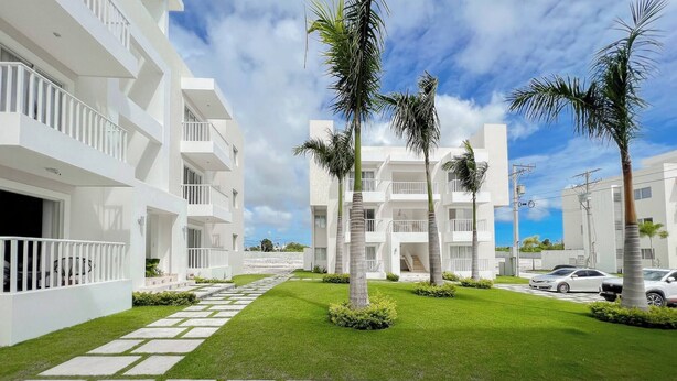 A modern building with white balconies, a well-maintained lawn, and palm trees. - Goistay Punta Cana Sol, Playa Pool 15 Min Airport (Punta Cana)