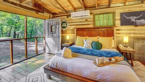 A wooden cabin bedroom with a bed, pillows, and a nightstand. - Unique Eureka Springs Cabin: Deck & Forest Views! (Busch)