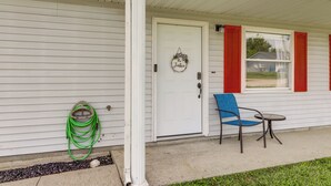 A house with a white exterior, a front door with a wreath, red shutters, a blue chair, and a small table.