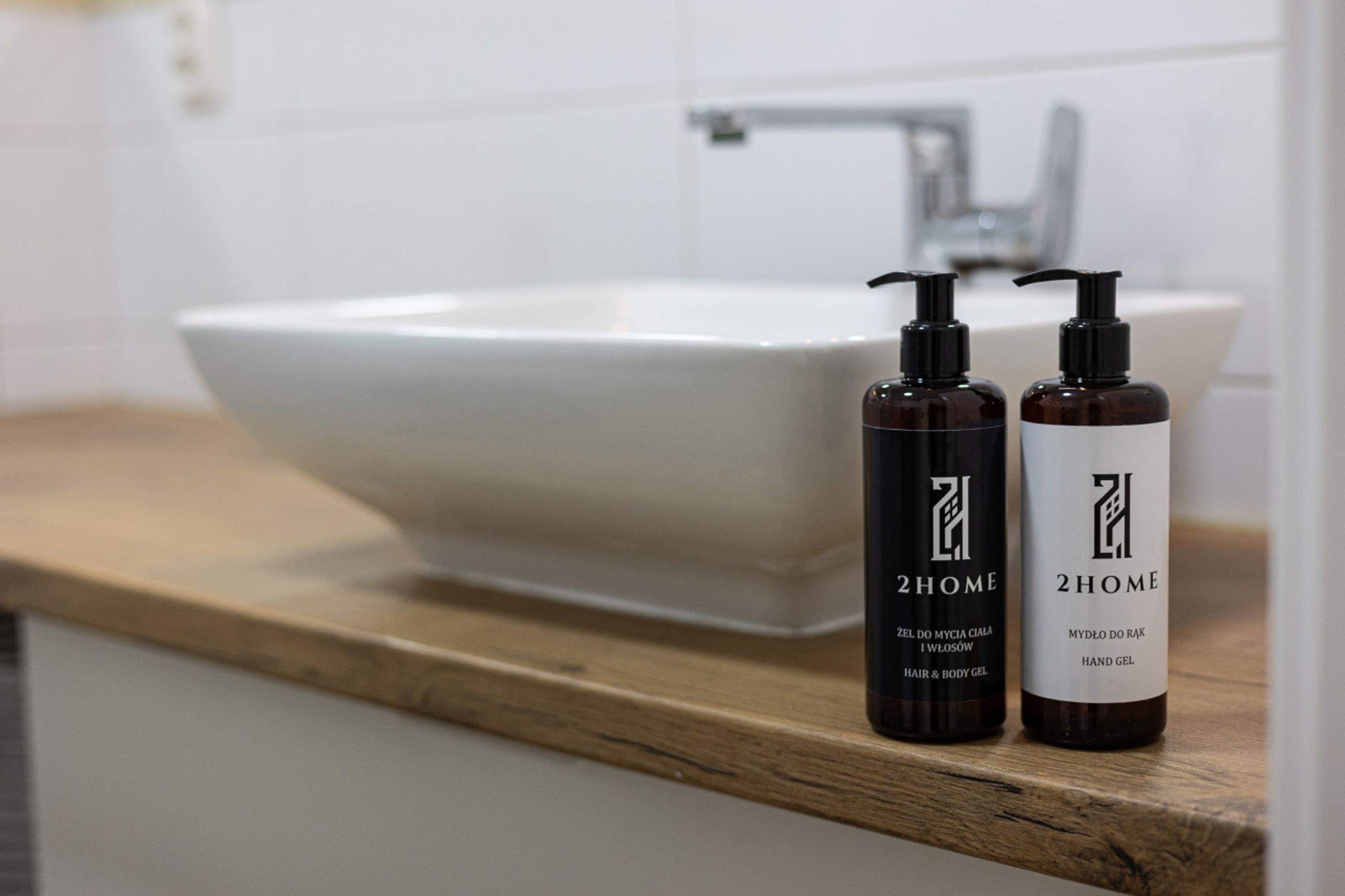 A bathroom with a white sink and two bottles of 2HOME hand gel on a wooden countertop.