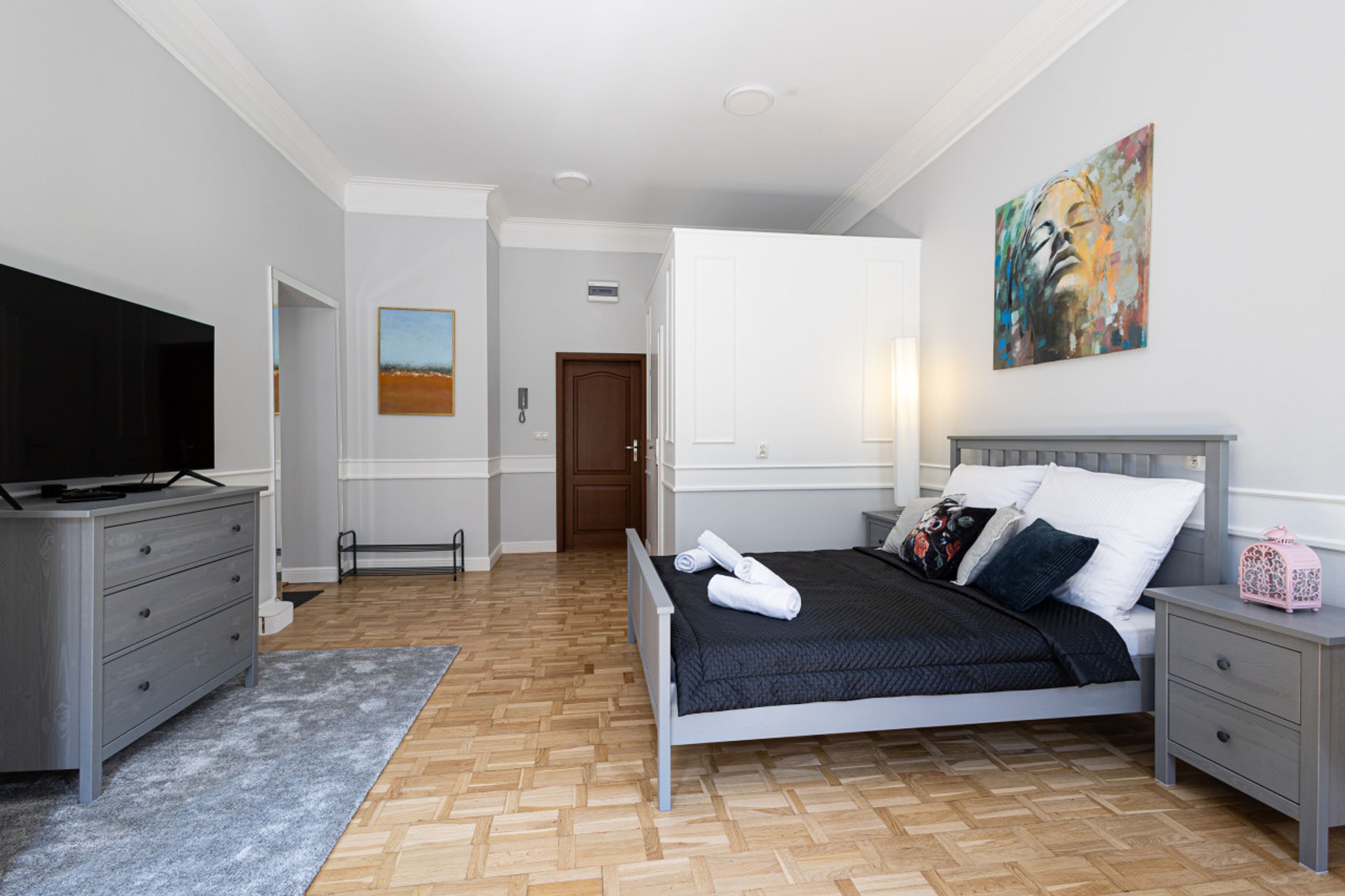 A bedroom with a bed, a TV, a dresser, and a painting on the wall.