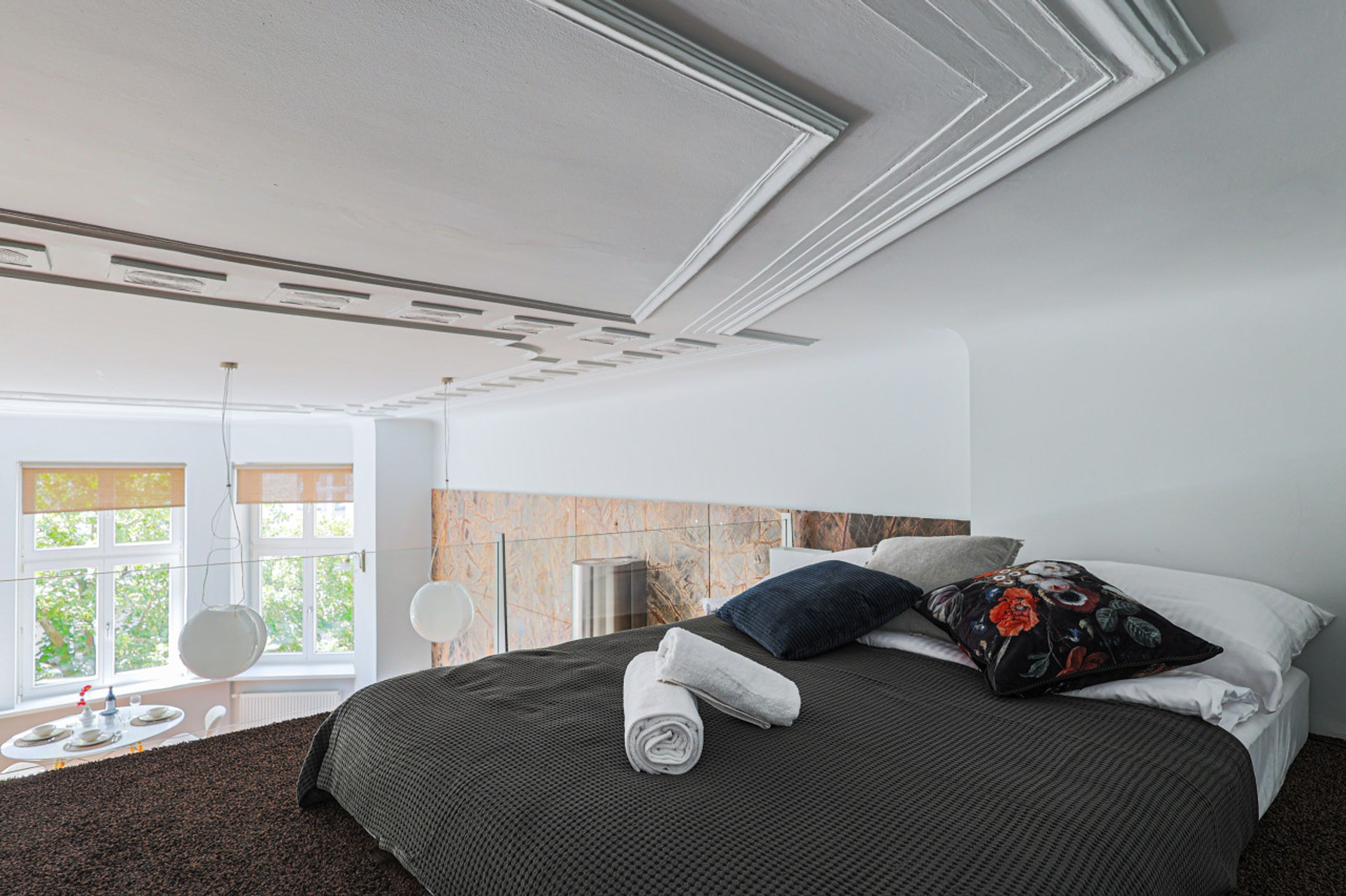 A modern hotel room with a large bed, a round mirror, and a view of greenery through the window.