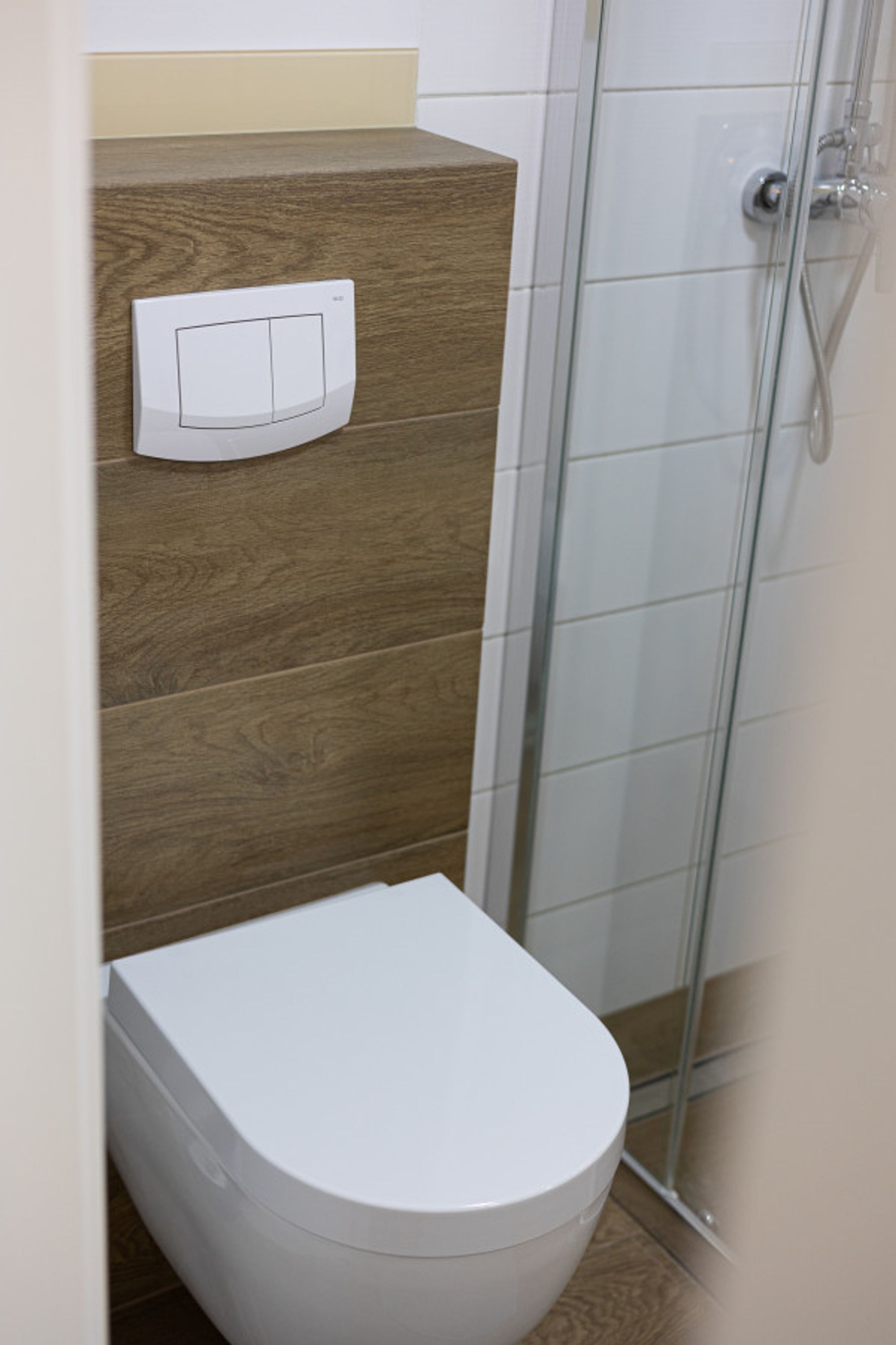 Un baño con inodoro blanco, tocador de madera y cabina de ducha con mampara de cristal.