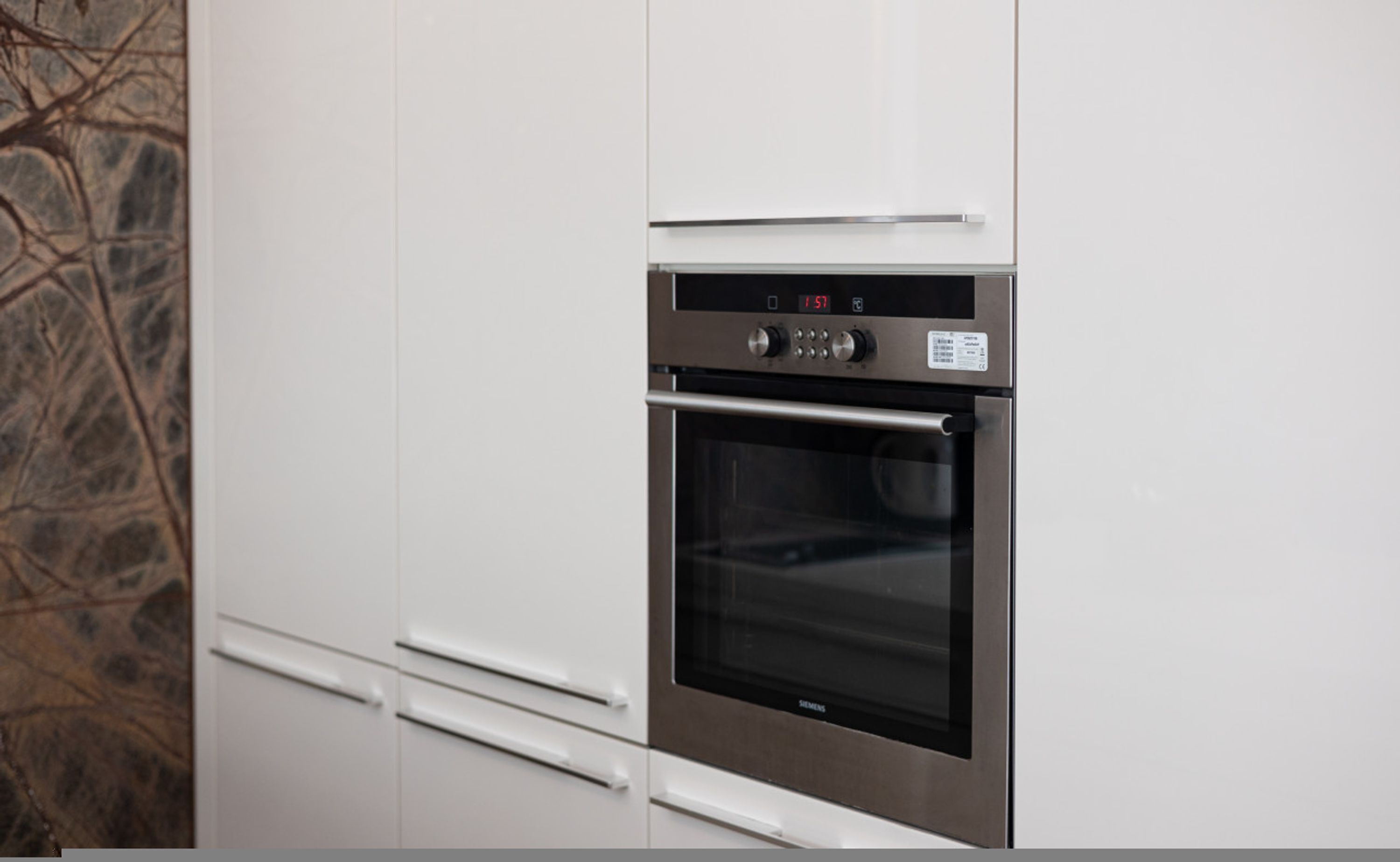 A stainless steel oven built into a white kitchen cabinet with a digital display and control knobs.