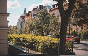 Vista de una calle con arquitectura europea tradicional, un coche rojo estacionado al costado, y un árbol en primer plano.