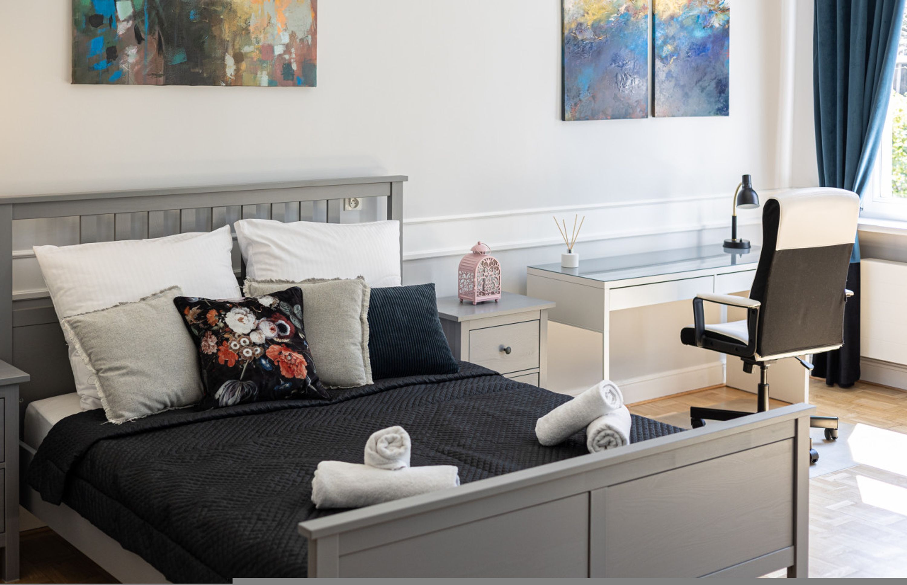 A neatly made bed with pillows, a bedside table with a lamp, a chair, and artwork on the wall.