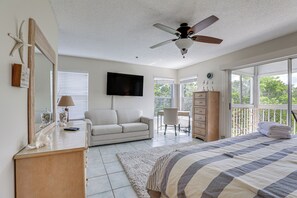 A bedroom with a bed, a ceiling fan, a TV, a dresser, a chair, and a window with a view of trees. - Holmes Beach Condo Near Anna Maria: Pool Access! (Holmes Beach)