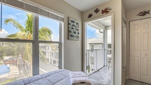 A bedroom with a large window, a bed with a striped bedspread, and a view of the outside. - Holmes Beach Condo Near Anna Maria: Pool Access! (Holmes Beach)