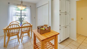 Een eethoek met een houten tafel en stoelen, een rieten mand met lekkernijen, en een wit kastje.