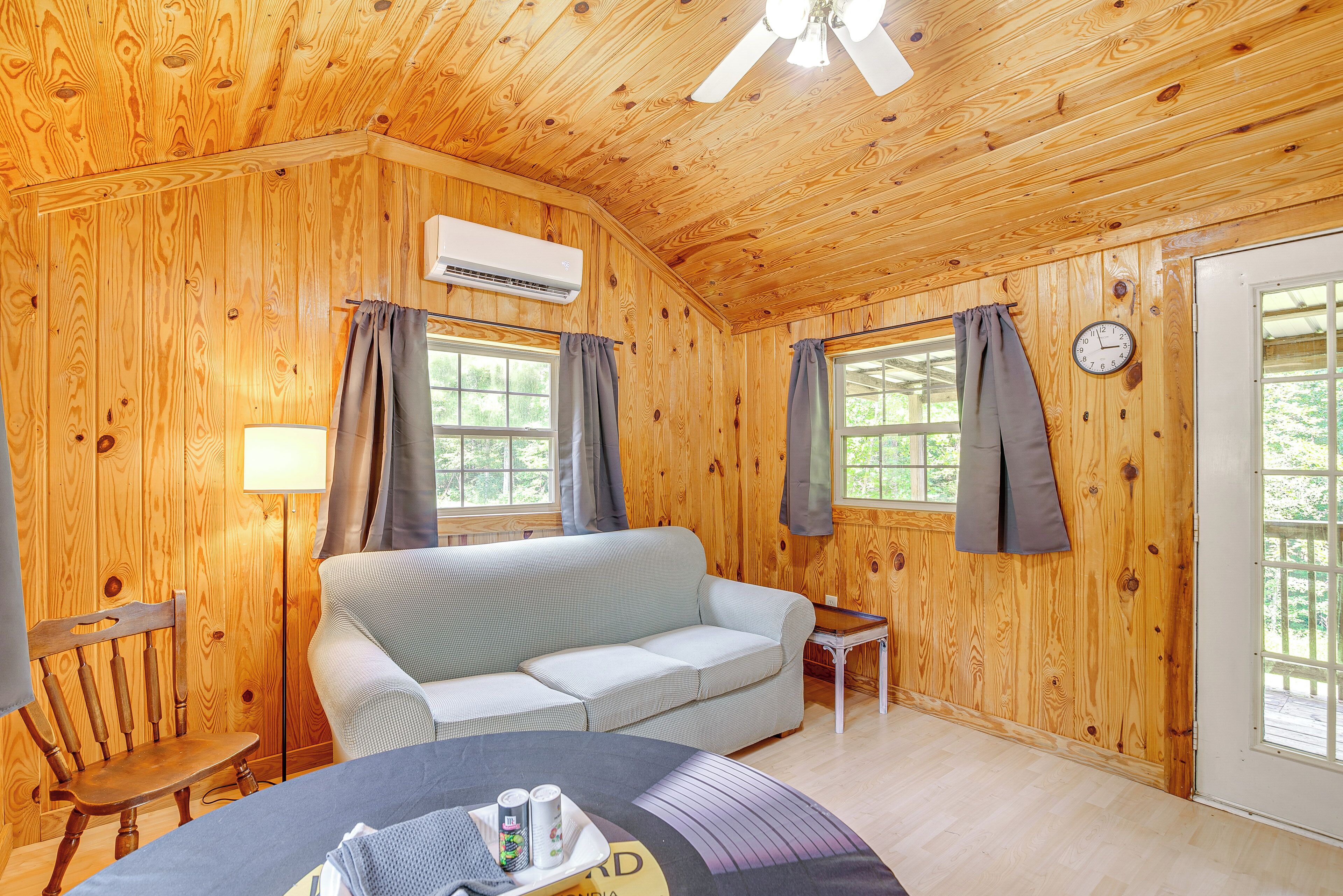 A wooden cabin room with a sofa, a small table, a chair, and a bed.