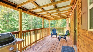 Una terraza de madera con una parrilla, dos sillas Adirondack y vistas a un bosque.