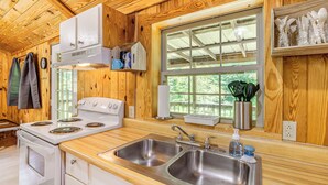 Cocina de cabaña de madera con estufa, lavamanos y ventana con vistas a la vegetación.