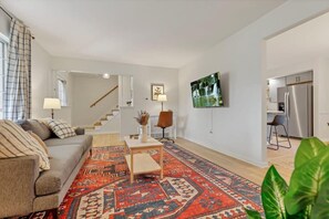 Una sala de estar con sofá, mesa de centro y alfombra estampada. Una escalera conduce a otro nivel.