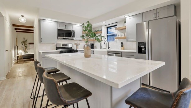 Een moderne keuken met een groot eiland, barkrukken, roestvrijstalen apparatuur en een potplant.