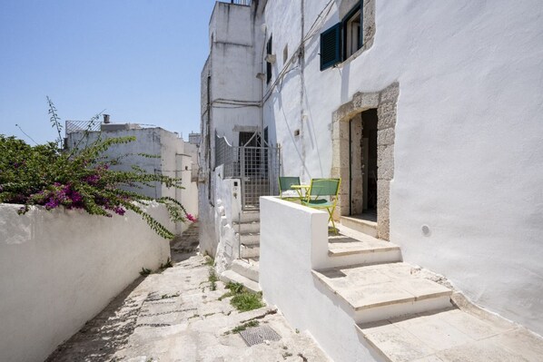 A narrow alleyway with white buildings, a green chair, and a door.
