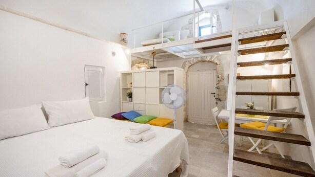 Ein Schlafzimmer mit einem Bett, einem weißen Ventilator, einer Treppe und einem kleinen Tisch mit Stuhl.