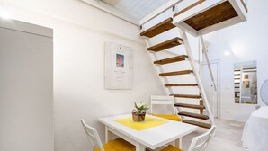 Ein weißer Tisch mit gelben Kissen, eine hölzerne Wendeltreppe und ein gerahmtes Zertifikat an der Wand.