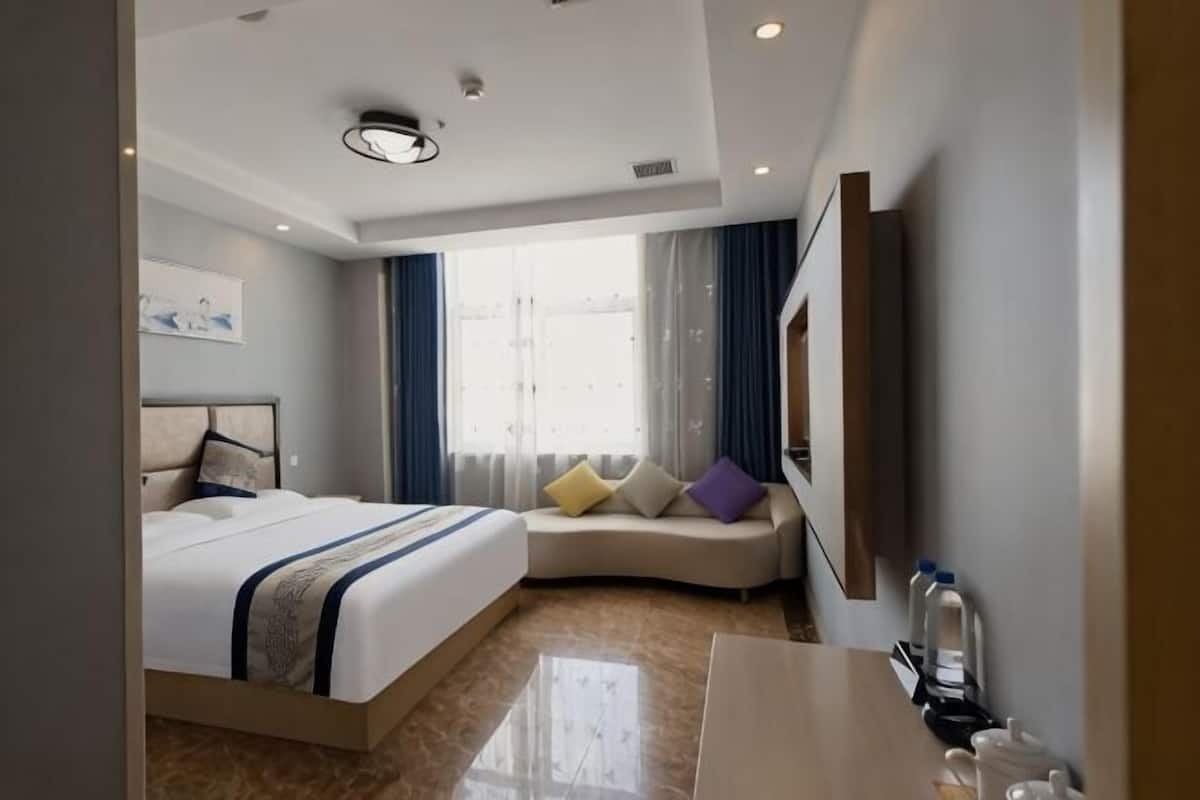 Habitación de hotel con cama, sofá, escritorio, televisor y ventana con cortinas.