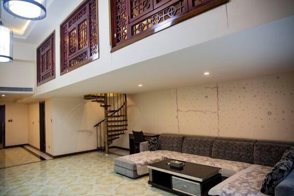 Amplia sala de estar con sofá, reposapiés y mesa de centro. Se observa una escalera al fondo.