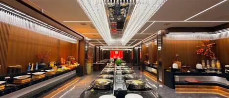 A hotel lobby with a long reception desk, a chandelier, and a buffet area.