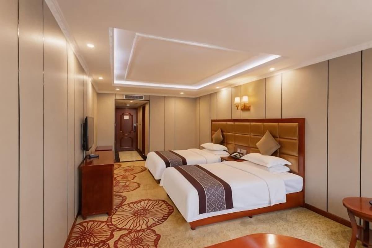 Habitació d'hotel amb dos llits, una taula de treball, una televisió i una catifes amb dibuixos florals.