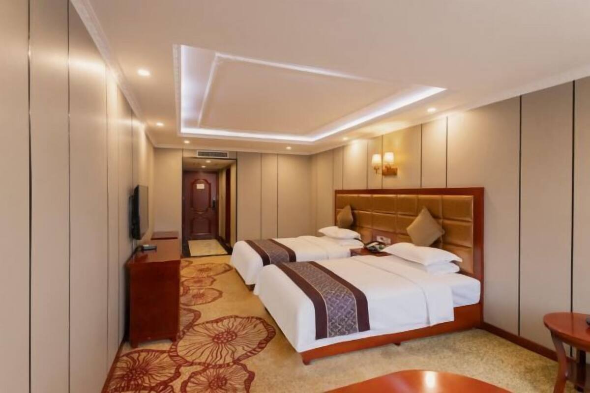 Habitación de hotel con dos camas, televisión, escritorio y piso alfombrado.