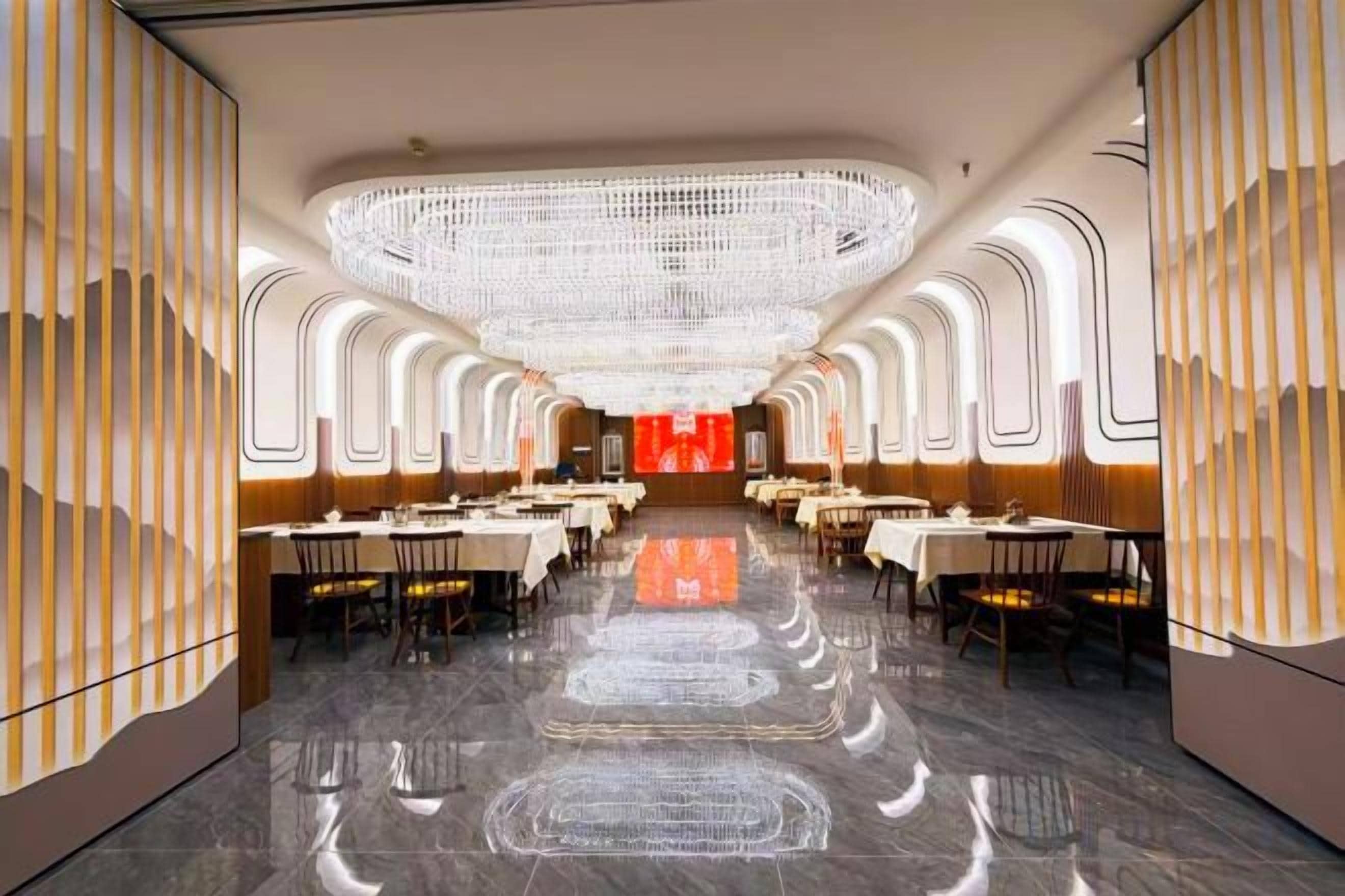 A spacious dining area with multiple tables and chairs, a central chandelier, and a reflective floor.