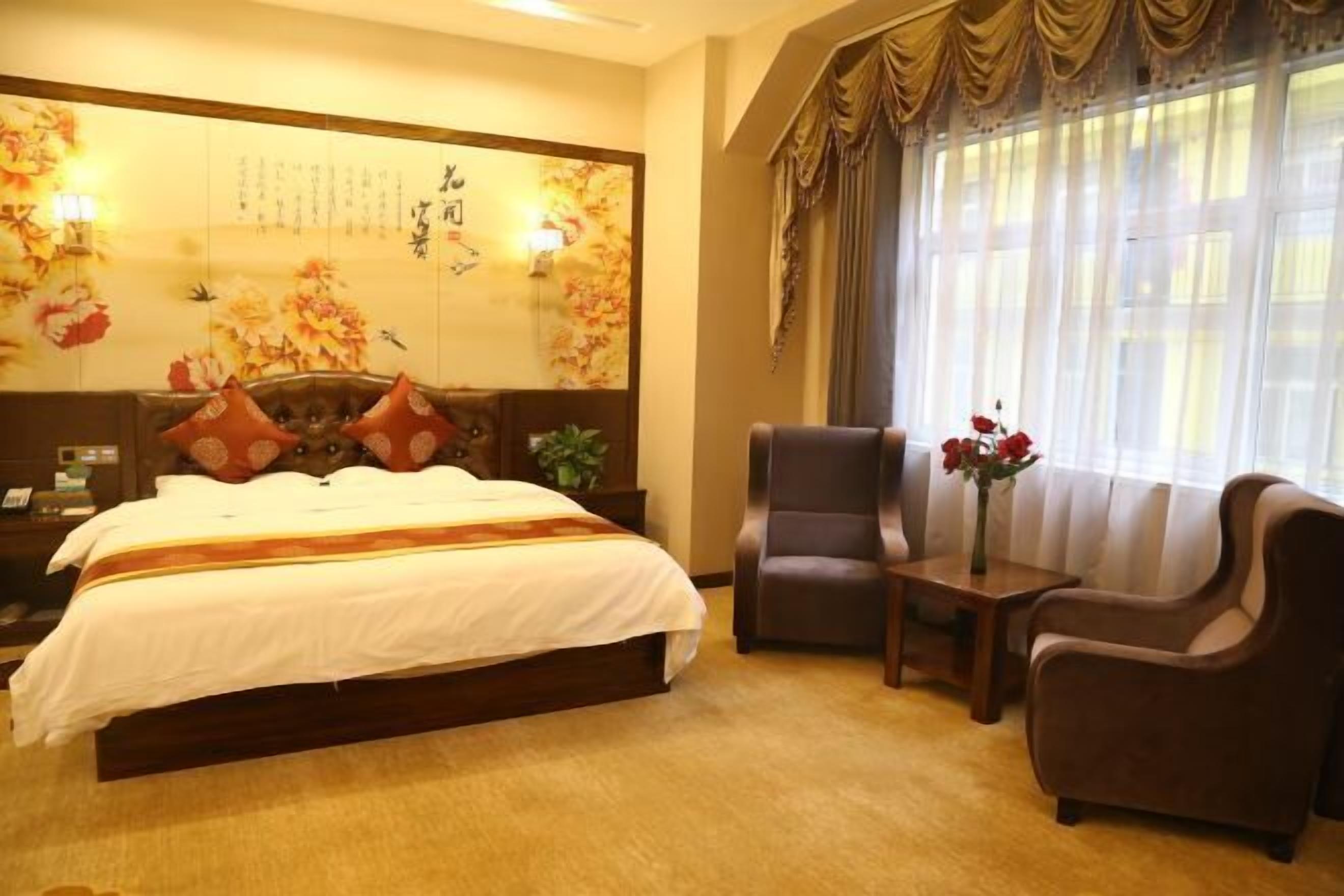 A hotel room with a large bed, two armchairs, a small table, and a decorative wall with calligraphy.