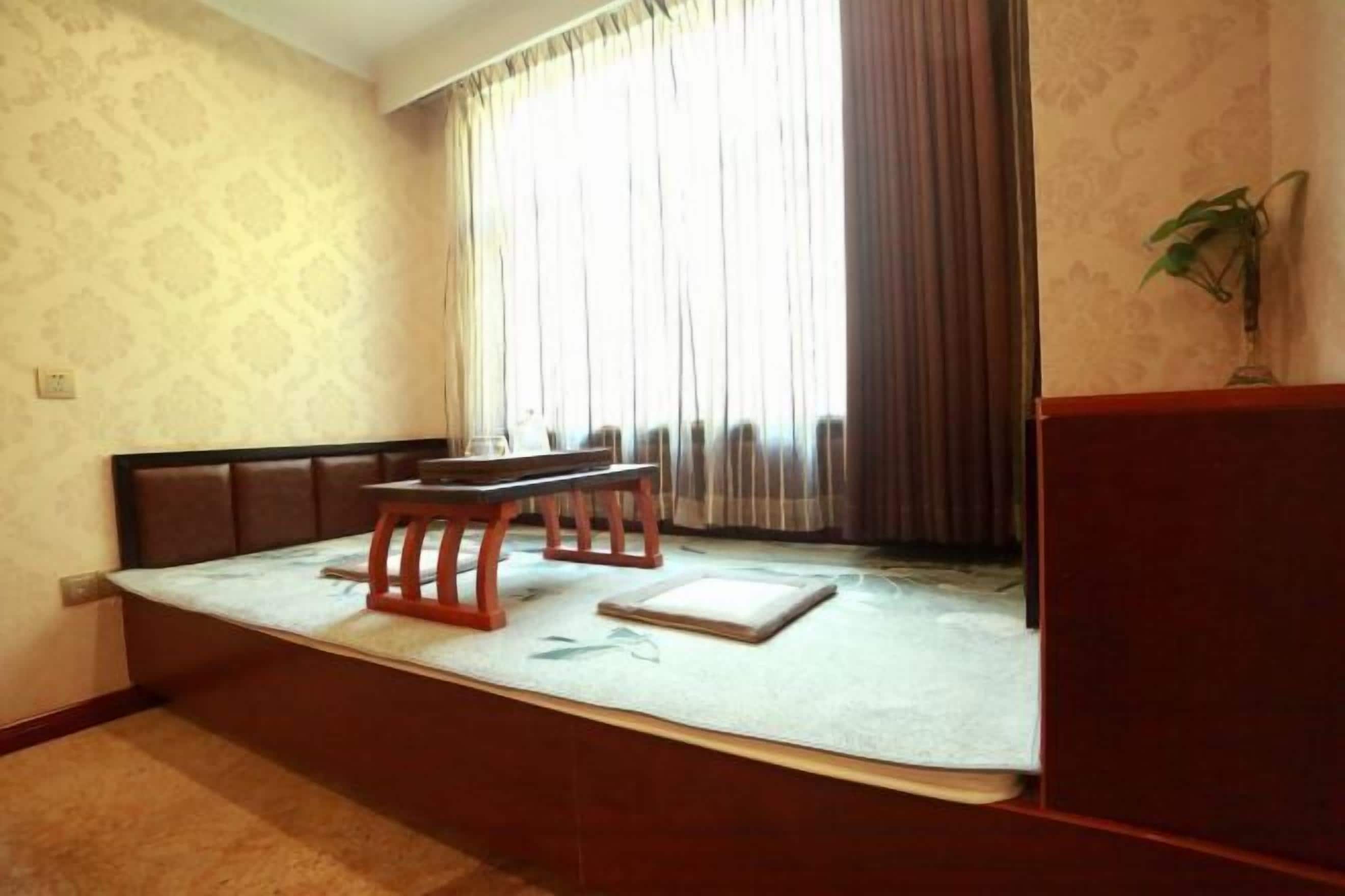A room with a bench and a table, a window with curtains, and a plant on a stand.