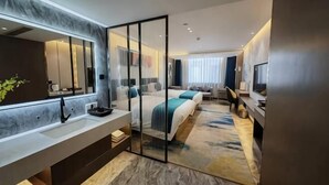 A modern hotel room with a large mirror, a bed with a blue and white duvet, a TV, and a desk with a chair. - Shiji Jiamei Hotel (Suide)